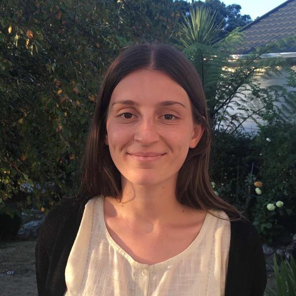 A person smiling at the camera with green foliage behind them